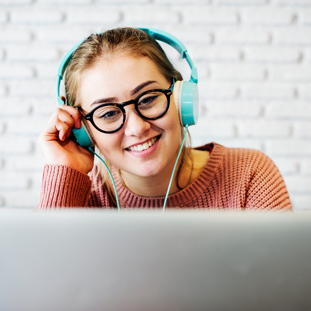 smiling woman wearing blue headphones with computer in foreground